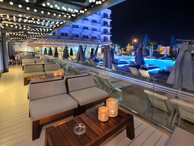 Night scene of a hotel terrace with seating, candles, and a lit pool in the background.