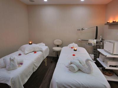 Zwei weiße Massageliegen mit Handtüchern und Kerzen in einem ruhigen, hellen Behandlungsraum.