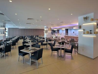 Modern, bright restaurant area with many tables and chairs in neutral colors.