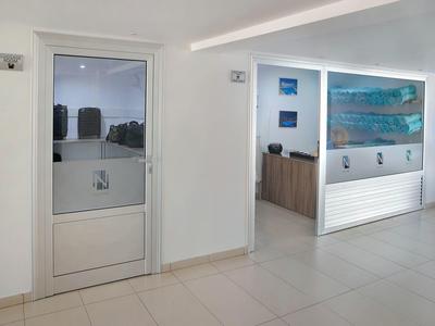 Moderner, heller Raum mit weißem Boden, Glastür und Empfangstresen mit Kunst an der Wand.