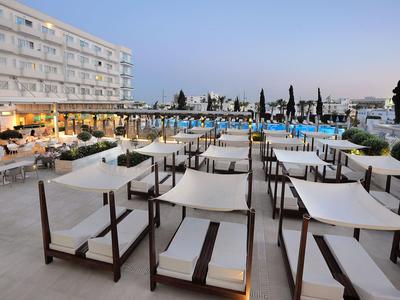 Open hotel pool area with lounge chairs and tables in the evening under clear sky.
