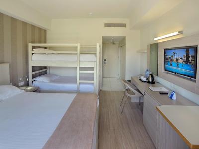 Hotelzimmer mit Einzelbett, Etagenbett, Schreibtisch, Wandfernseher und heller Holzmöblierung.