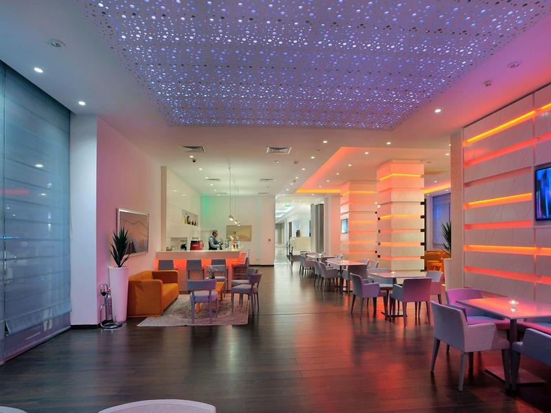 Moderner Gastraum mit bunten LED-Leuchten, weißen Möbeln und dunklem Holzboden.