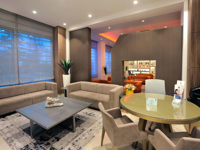 Moderner Wohnraum mit großen Fenstern, grauen Sofas, rundem Tisch und warmem Licht innen.