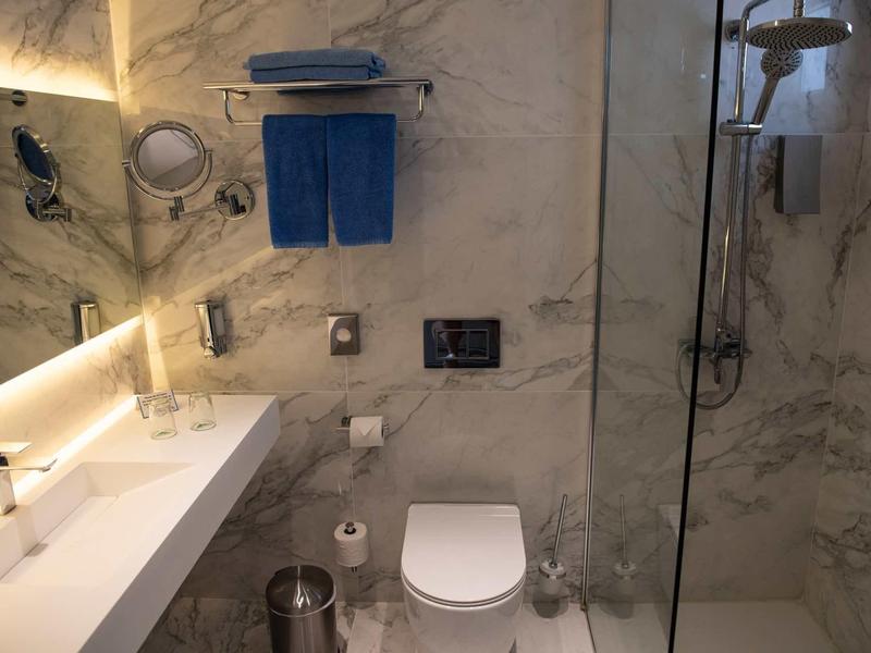 Kleine moderne Badezimmereinrichtung mit Marmorwänden, weißen Waschbecken und blauen Handtüchern.