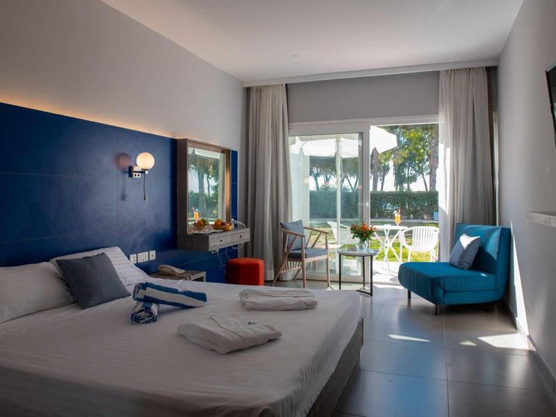 Modernes Hotelzimmer mit Doppelbett, blauer Wand, Sitzgelegenheiten und großer Glasfront zum Außenbereich.