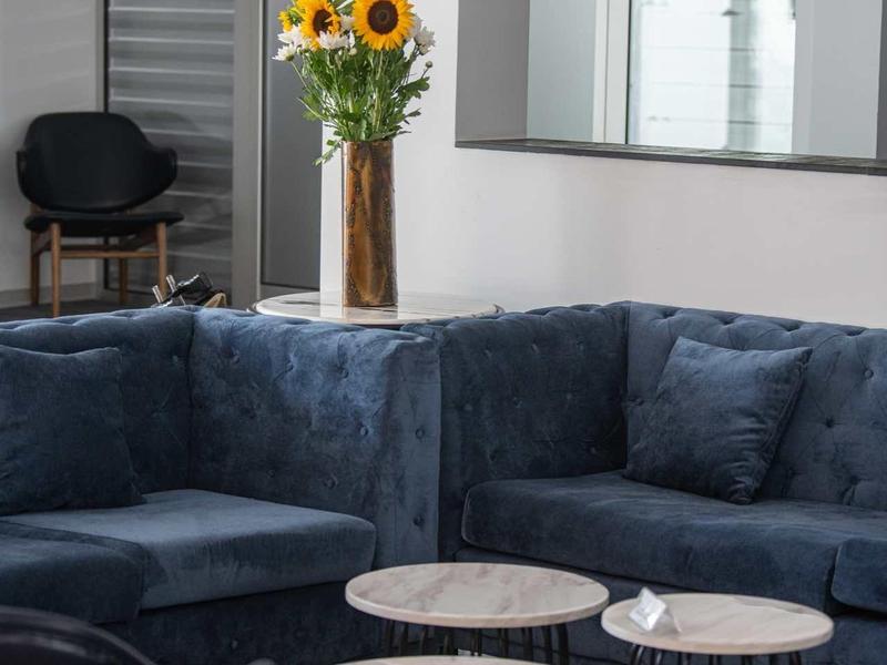 Modernes Wohnzimmer mit dunkelblauem Samtsofa, zwei kleinen runden Tischen und einem Blumenstrauß mit Sonnenblumen.