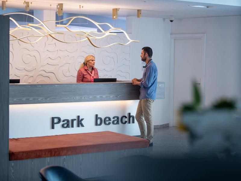 Moderne Hotellobby mit beleuchtetem Empfangstresen, Rezeptionistin und Gast im Gespräch.