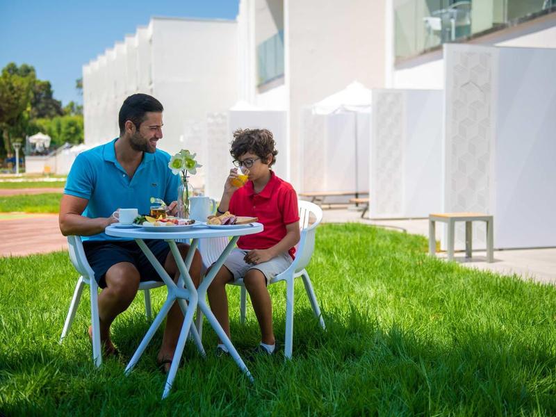 Mann und Junge sitzen draußen an weißem Tisch auf grünem Rasen und essen gemeinsam.