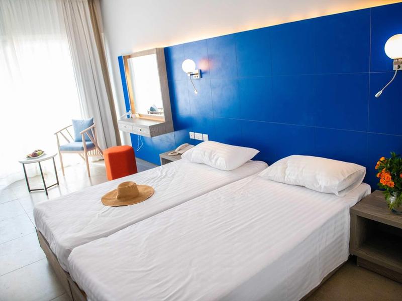 Zwei Einzelbetten mit weißen Bezügen, blauer Wand im Hintergrund, ein kleines Sofa und Fenster mit Vorhängen.