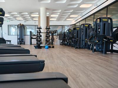 Moderne Fitnessstudio mit Laufbändern, Kraftgeräten und Hanteln auf hellem Holzfußboden.