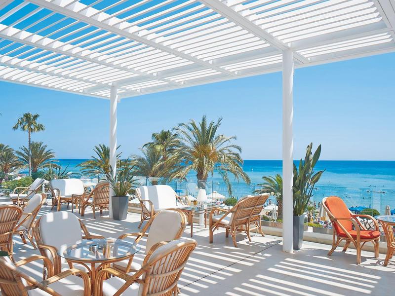 Sonnenterrasse mit weißen Holzlatten, Rattanmöbeln und Meerblick bei klarem Himmel.