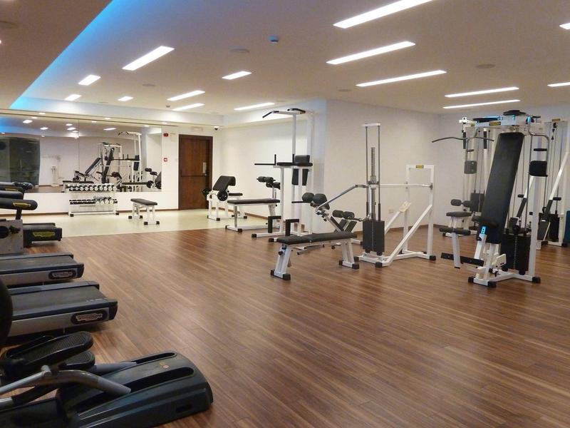 Großer Fitnessraum mit Holzboden, modernen Geräten und Spiegelwand an einer Seite.