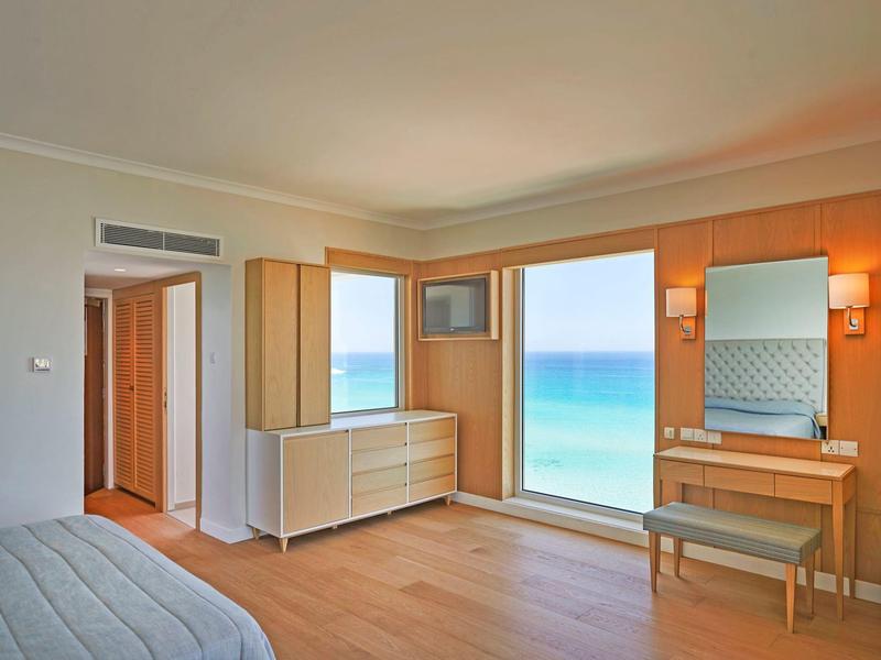 Hell eingerichtetes Schlafzimmer mit Holzboden, großem Fenster zum Meer und modernem Möbelstück.