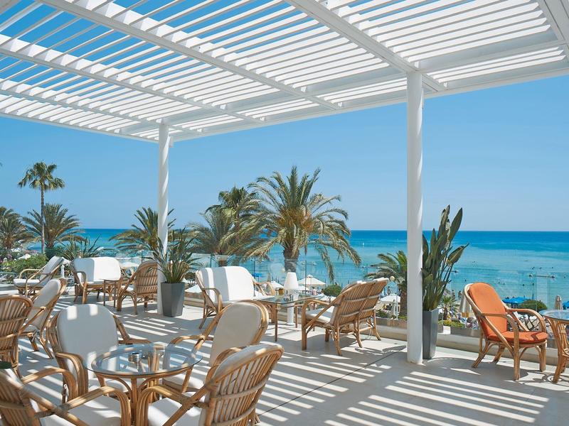 Offener Strandterrassenbereich mit runden Tischen, Stühlen, Palmen und Blick auf das blaue Meer.