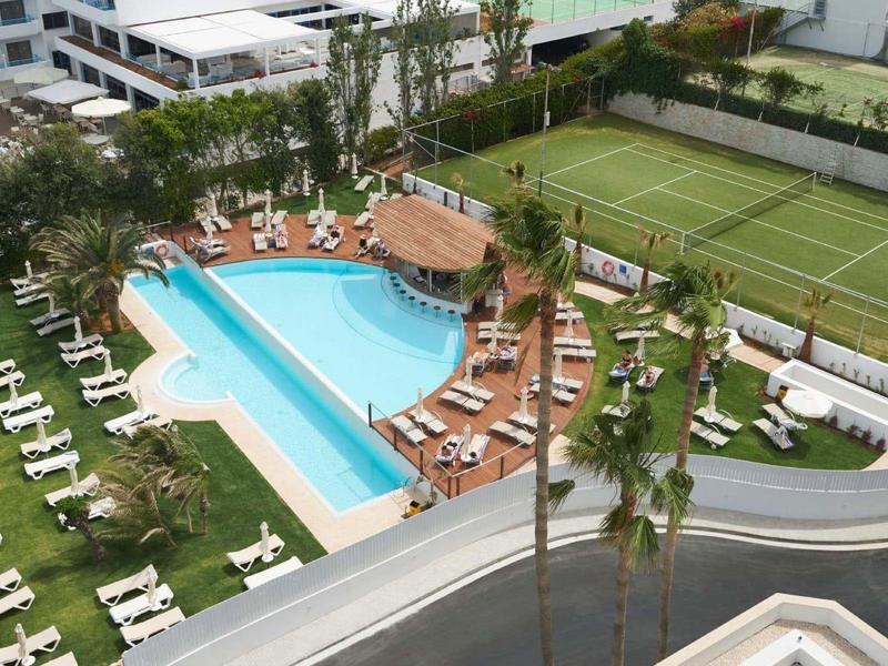 Großer Außenpool mit Liegestühlen neben Tennisplatz und Grünflächen in einem Wohnkomplex.