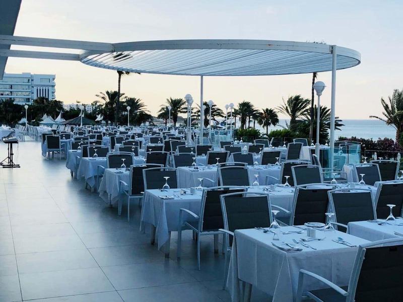 Große Terrasse mit vielen gedeckten Tischen und Stühlen unter modernem Sonnenschutz am Meer.