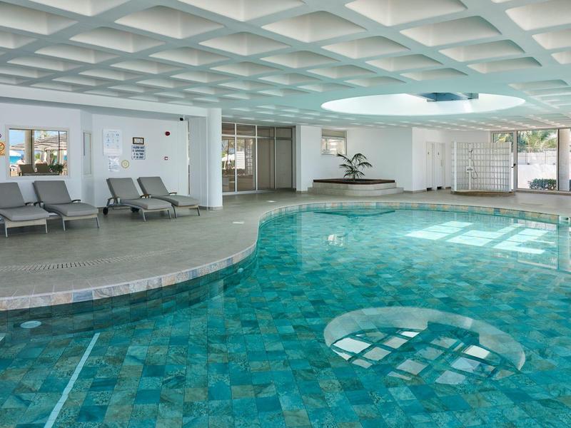 Innenpool mit blauen Fliesen, Liegestühlen und großen Fenstern in einem Hotel.