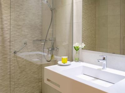 Modernes Badezimmer mit weißem Waschbecken, großem Spiegel und Duschbereich mit Glaswand.