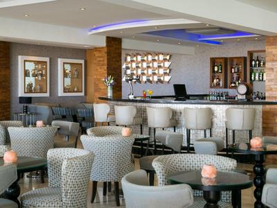 Moderne Hotelbar mit vielen gepolsterten Sesseln und einem beleuchteten Deckenakzent.