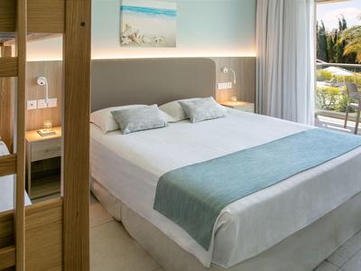 Helles Hotelzimmer mit Doppelbett, Nachttischen, Balkon und Blick auf Bäume.