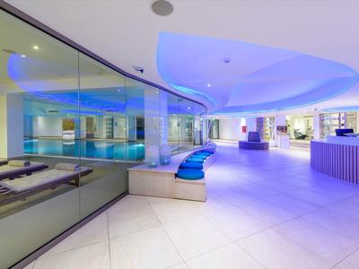 Moderner Wellnessbereich mit blauer Beleuchtung, Lounge-Sesseln und Schwimmbad mit Glasabtrennung.