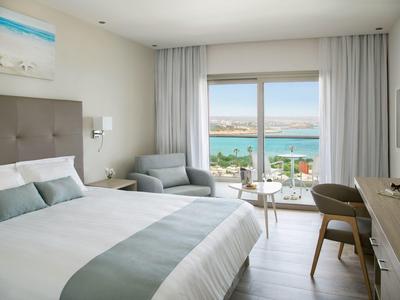 Modernes Hotelzimmer mit Doppelbett, Sitzbereich und Blick auf das Meer durch große Fenster.