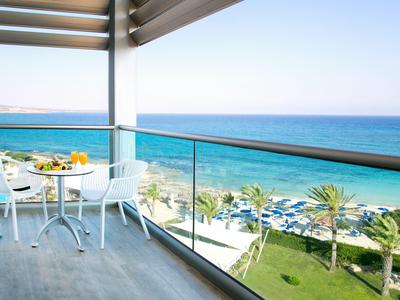 Balkon mit Tisch und Stühlen mit Blick aufs Meer und einen Garten mit Palmen.