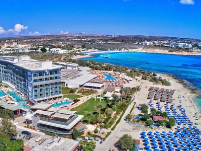 Luxushotel an der Küste mit Pool, Sonnenschirmen und klarem blauem Meer bei sonnigem Wetter.