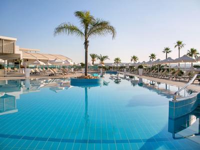 Moderner Pool mit Palmen, Liegestühlen und klar blauem Wasser bei sonnigem Wetter.
