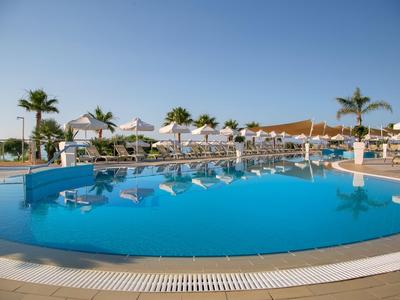 Großer Hotelpool mit Liegen und Sonnenschirmen unter klarem blauem Himmel.