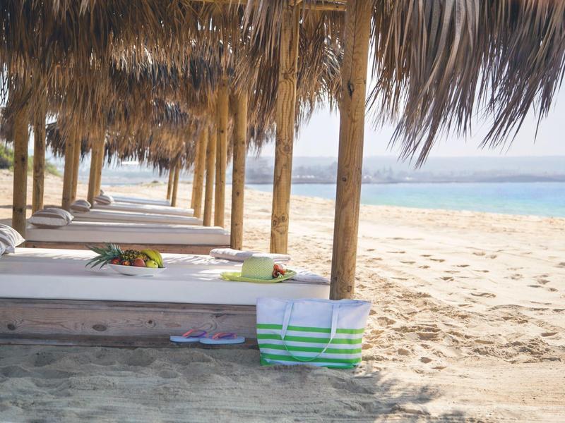 Reihen von Holzliegen unter Palmen auf einem Sandstrand mit Blick aufs Meer