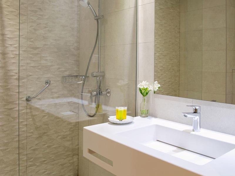 Modernes Badezimmer mit weißem Waschbecken, großem Spiegel und Duschbereich mit Glaswand.