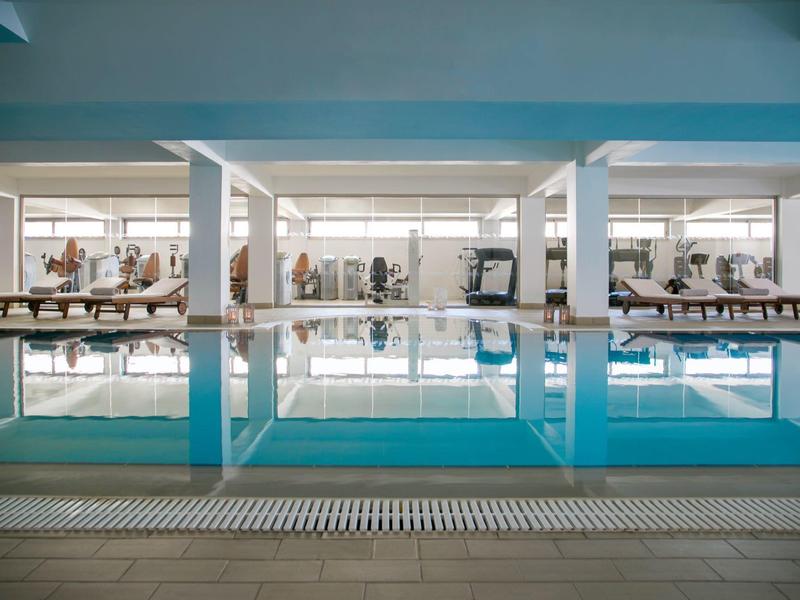 Moderner Innenpool mit Liegestühlen und Fitnessgeräten im Hintergrund.