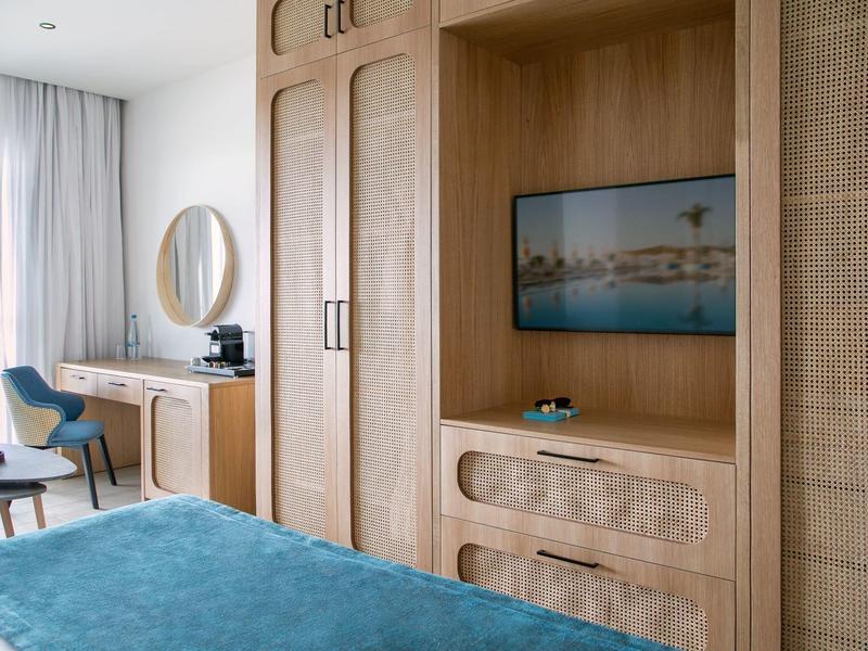 Hotelzimmer mit Holzmöbeln, Bett mit blauem Bettüberwurf und Fernseher an der Wand.