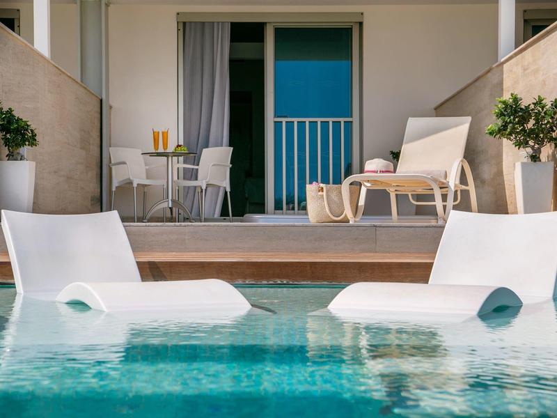 Zwei weiße Liegestühle im Pool vor einer modernen Hotelterrasse mit Stühlen und Pflanzen