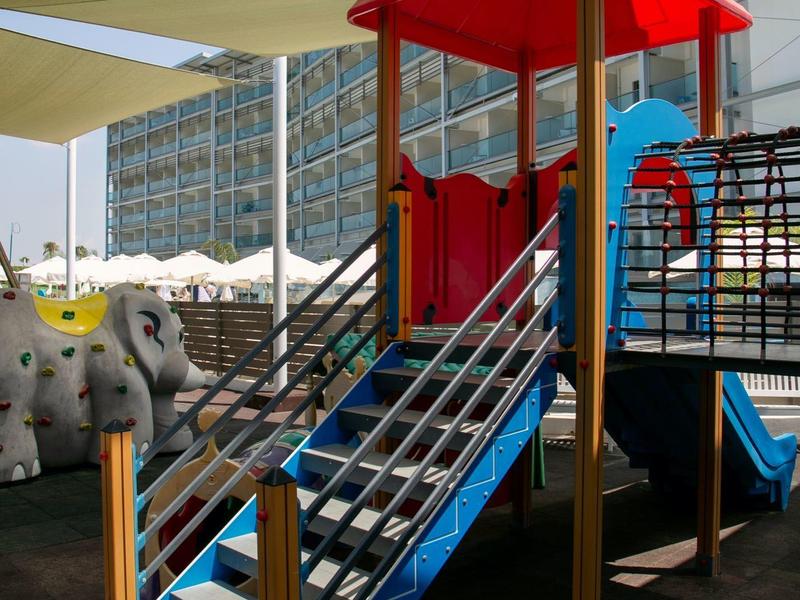 Bunter Kinderspielplatz mit Rutsche und Klettergerüst neben einem Hotelgebäude.
