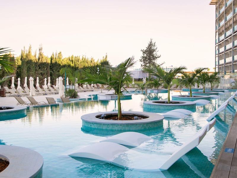 Pool mit Wasserliegen und Palmen neben einem Hotelgebäude in der Dämmerung.