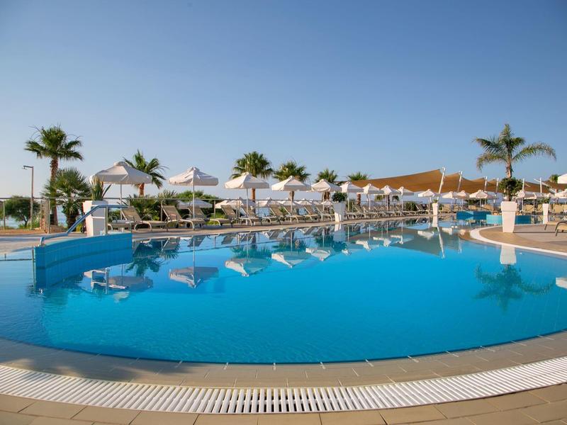 Runder Hotelpool mit Liegen, Sonnenliegen und Palmen unter blauem Himmel.