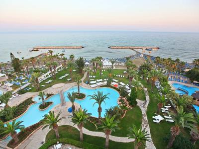 Vista di un resort con piscine, palme e lettini vicino al mare al tramonto.