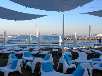 Area spiaggia con lettini bianchi e ombrelloni accanto a un mare calmo.