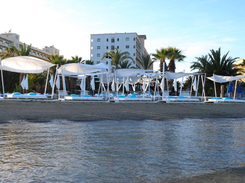 Strand mit weißen Sonnenschirmen, Palmen und Hotels im Hintergrund bei klarem Himmel.