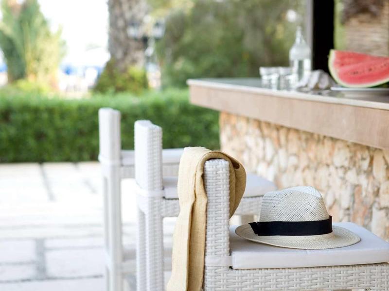 Weiße Holzstühle und Tisch mit Hut und Tuch an einem Steinmauer-Balkon unter Dach.