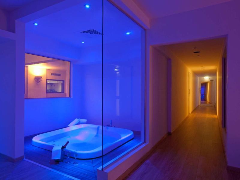 Moderner Flur mit Holzboden, rechts Türen, links großer Glasraum mit blauer Beleuchtung und Whirlpool.
