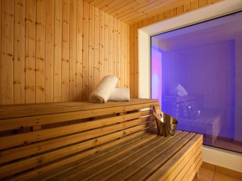 Sauna mit Holzbänken, Holzverkleidung, Handtuch und großer Glaswand mit blauem Licht dahinter.