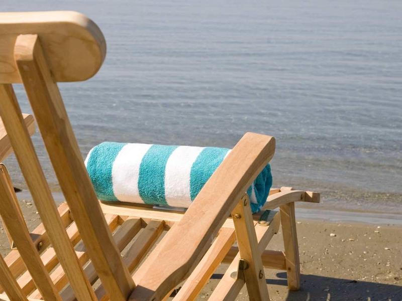 Holzliegestuhl mit blau-weiß gestreiftem Handtuch am ruhigen Strand mit ruhigem Meer.