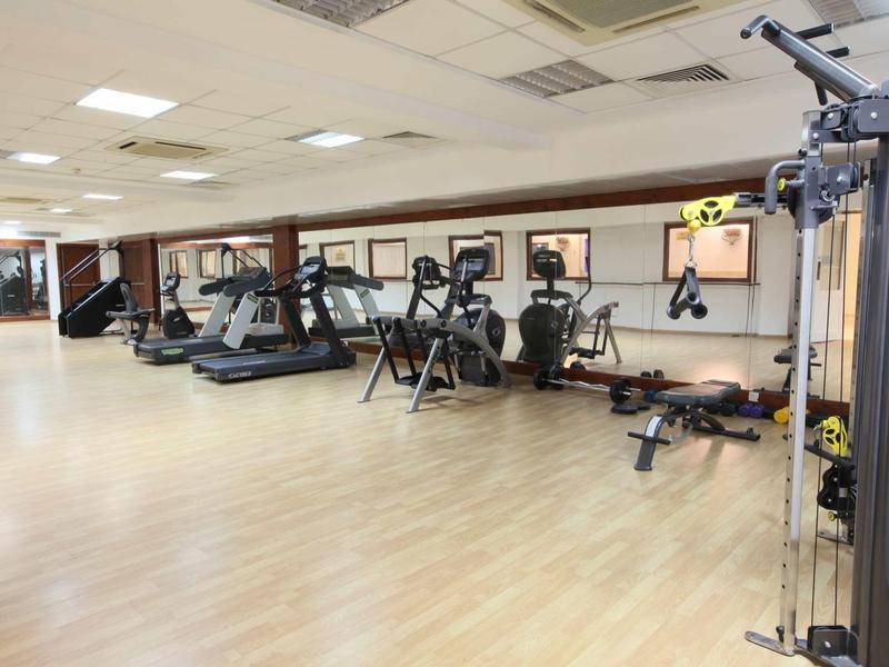 Großer Fitnessraum mit Laufbändern, Fahrrädern und Kraftgeräten auf hellem Holzboden.