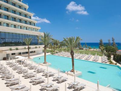 Piscina moderna dell'hotel con lettini e palme, vista sul mare blu sotto un cielo limpido.