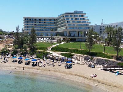 Hotel moderno a più piani vicino a una spiaggia di sabbia con lettini e acqua limpida.