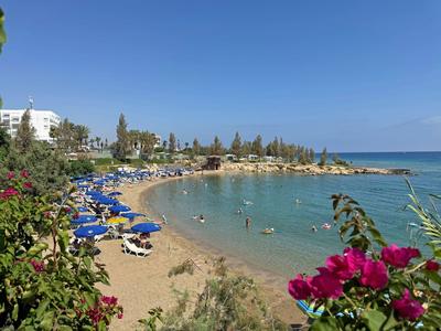 Zandstrand met blauwe ligstoelen en mensen in helder water onder een blauwe lucht